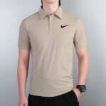 Beige polo shirt with a small black Nike swoosh logo worn by a man standing against a gray background.