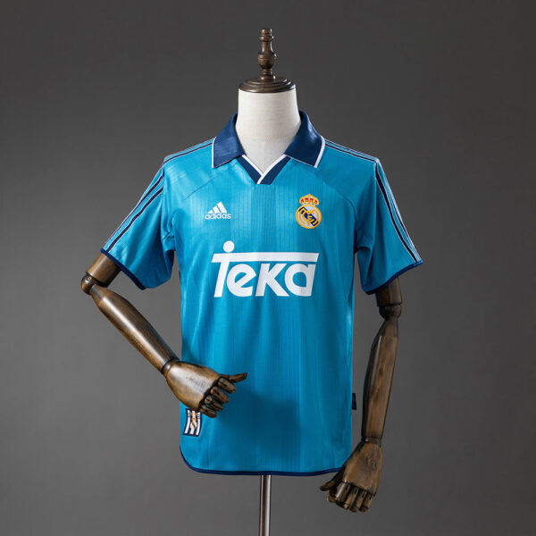 Real Madrid away jersey in teal on a mannequin, featuring TEKA sponsor and Adidas logo.