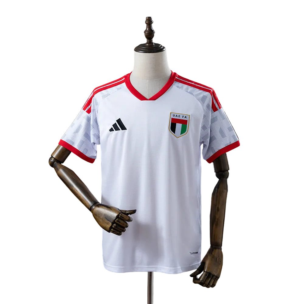 c7bec753 White UAE FA soccer jersey on a mannequin with red trim at the neck and sleeves, Adidas logo visible on the chest.