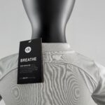 Black mannequin torso wearing a light gray shirt with a Nike BREATHE tag attached, highlighting DRI-FIT fabric details.