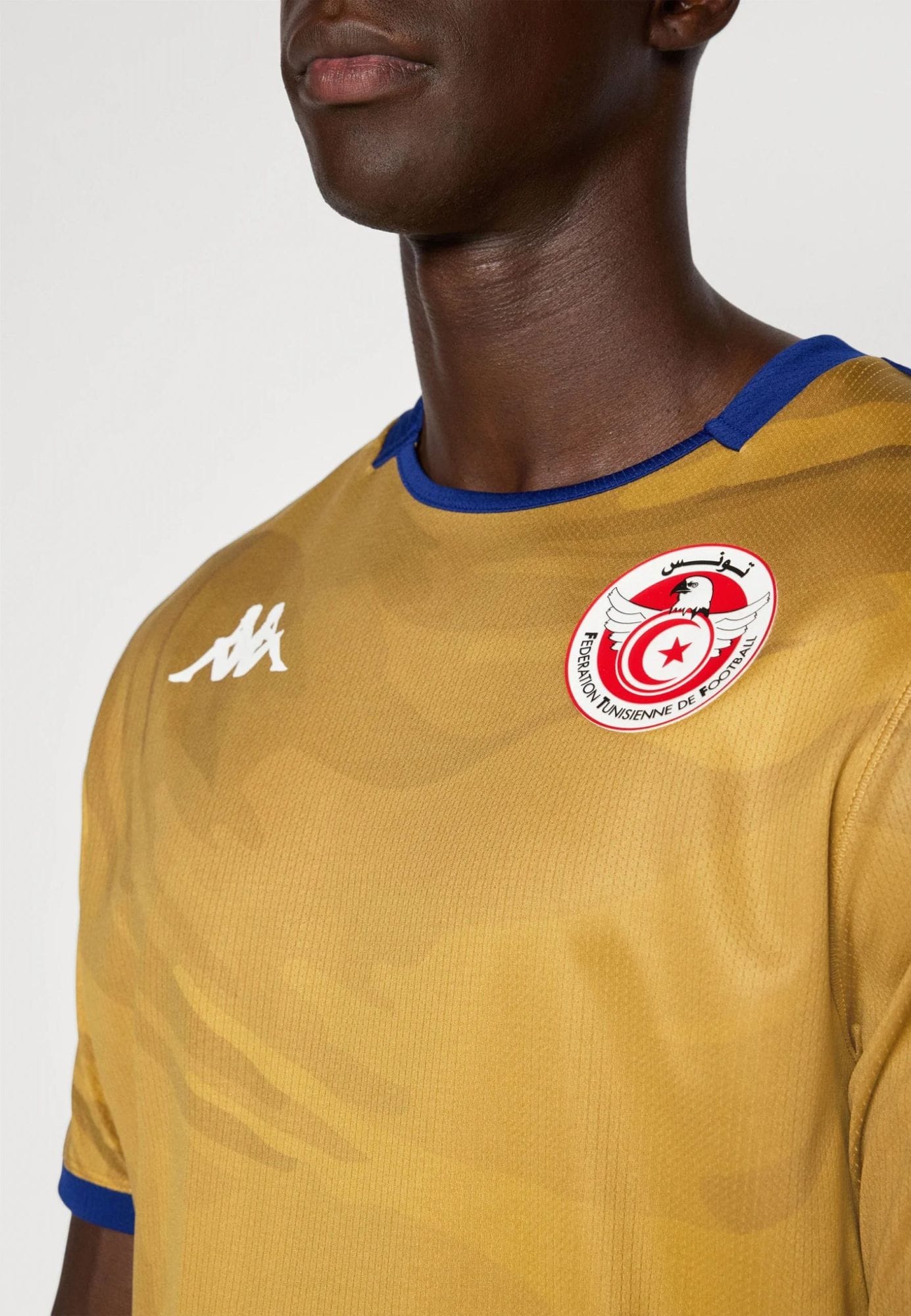 c84dd78ecde041c88fa071623bee266c | UAE SPORT STORE Close-up of a person wearing a mustard-yellow athletic jersey with blue trim showing a circular Tunisian Football Federation badge on the chest.