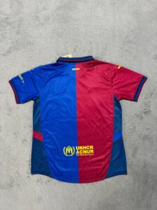 Back view of a blue-and-red split athletic jersey on a gray surface, featuring a yellow UNHCR/ACNUR logo near the bottom hem and a small tag at the collar side