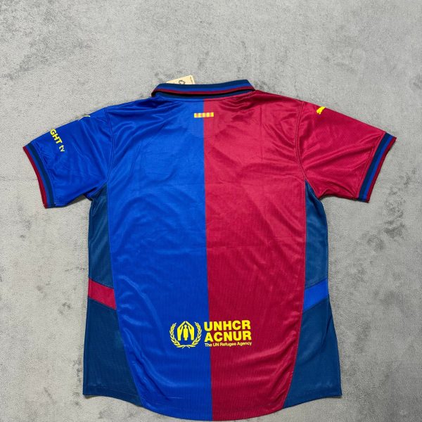 Back view of a blue-and-red split athletic jersey on a gray surface, featuring a yellow UNHCR/ACNUR logo near the bottom hem and a small tag at the collar side