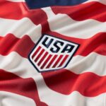 Close-up of a USA shield patch on a red and white striped sports jersey, showing blue outline and stripes in the emblem area.