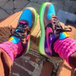 Colorful sneakers with blue, pink, purple, and neon green accents worn with bright pink socks, resting on a brick ledge.