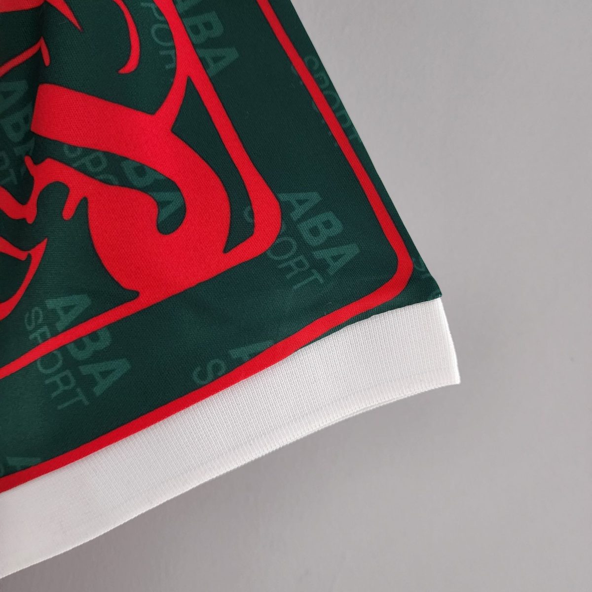 Close-up of dark green fabric with a bold red graphic and a white ribbed hem, likely part of a sports jersey or hoodie edge.