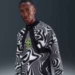 c8cdc6b7-d951-4495-b37d-bd343b34b446 | UAE SPORT STORE Portrait of a person wearing a bold black-and-white swirl-pattern Brazil jersey with a neon green crest on the chest.