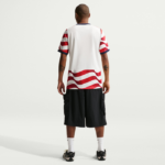 Man standing with back to camera, wearing a white T-shirt with red wave pattern and black cargo shorts.