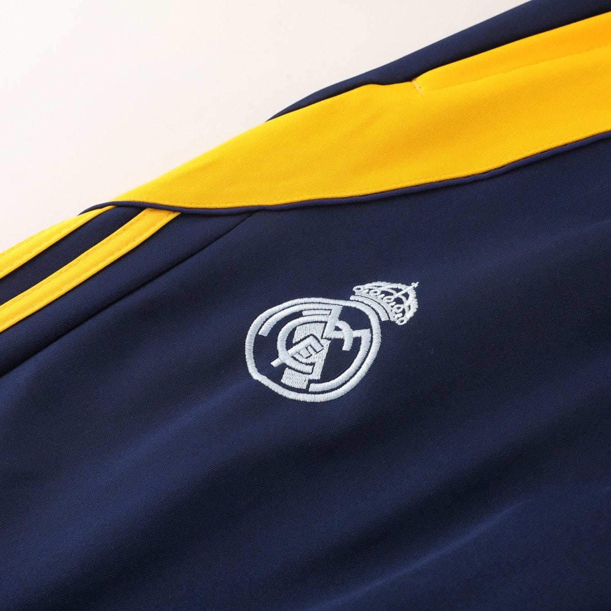 Close-up of a navy backpack with a bright yellow zipper and white embroidered crest, on a dark fabric.