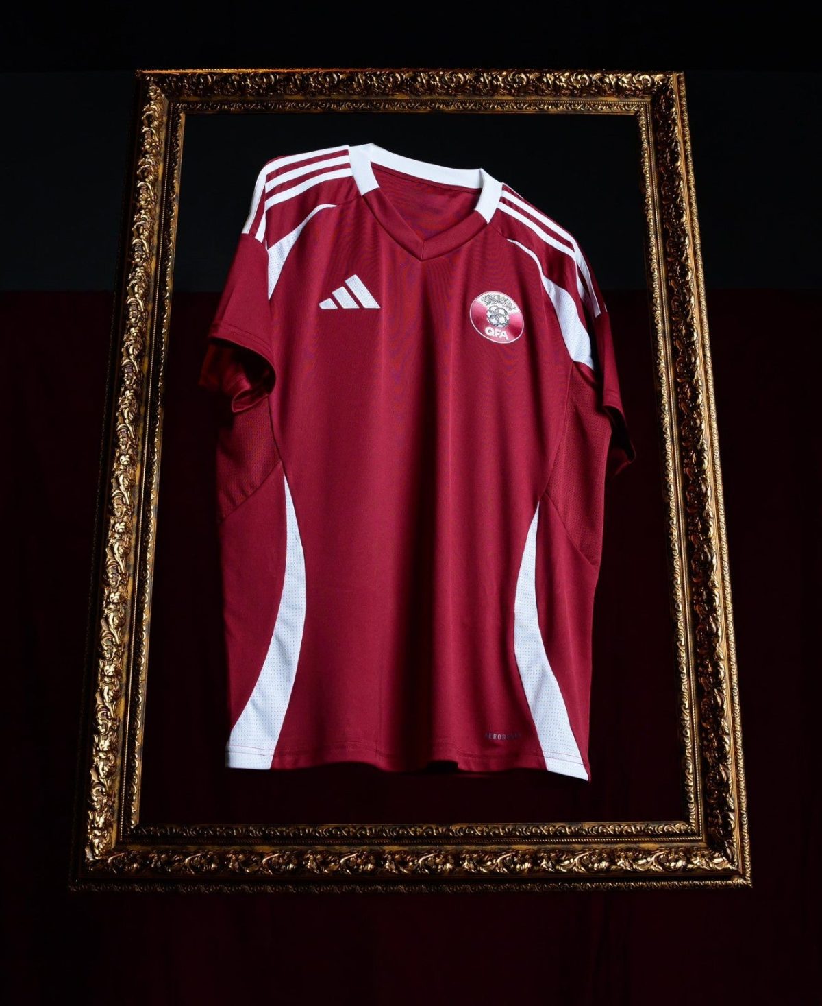 Maroon soccer jersey with white accents framed inside an ornate gold frame against a dark background.