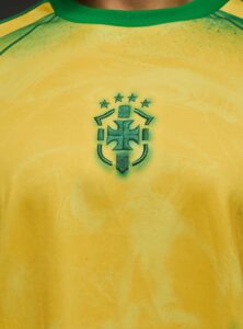 Embroidered green crest on a bright yellow soccer jersey with a green collar, centered on the chest.