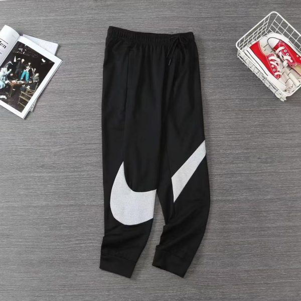 Black joggers with a large white Nike swoosh on the left leg, laid on a gray wooden floor.