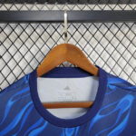 Blue Adidas athletic jersey with flame pattern on a wooden hanger against a metal lattice background.