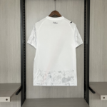 White short-sleeve T-shirt on a hanger in a closet; light gray pattern on sleeves and bottom pocket; 'Kidsuper' logo at the back of the neck.