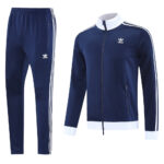 Navy blue Adidas tracksuit jacket with white collar and stripes, shown with matching navy pants featuring white side stripes.