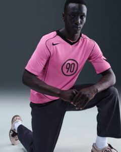 Soccer player in a pink jersey with the number 90, kneeling in a studio pose against a dark backdrop.