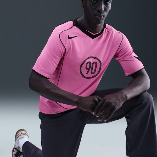 Soccer player in a pink jersey with the number 90, kneeling in a studio pose against a dark backdrop.