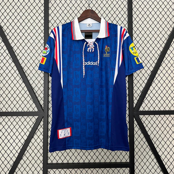 Blue adidas football jersey on a hanger with a lace-up collar, red-white trim, and patches on the sleeves; dark blue panels and subtle pattern throughout.