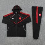 Liverpool FC black training tracksuit laid flat on a gray carpet, jacket with red piping and crest, matching pants with red stripes.