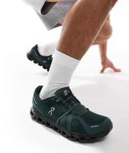 Athlete wearing dark green On running shoes and white crew socks in a starting lunge position, ready to sprint.