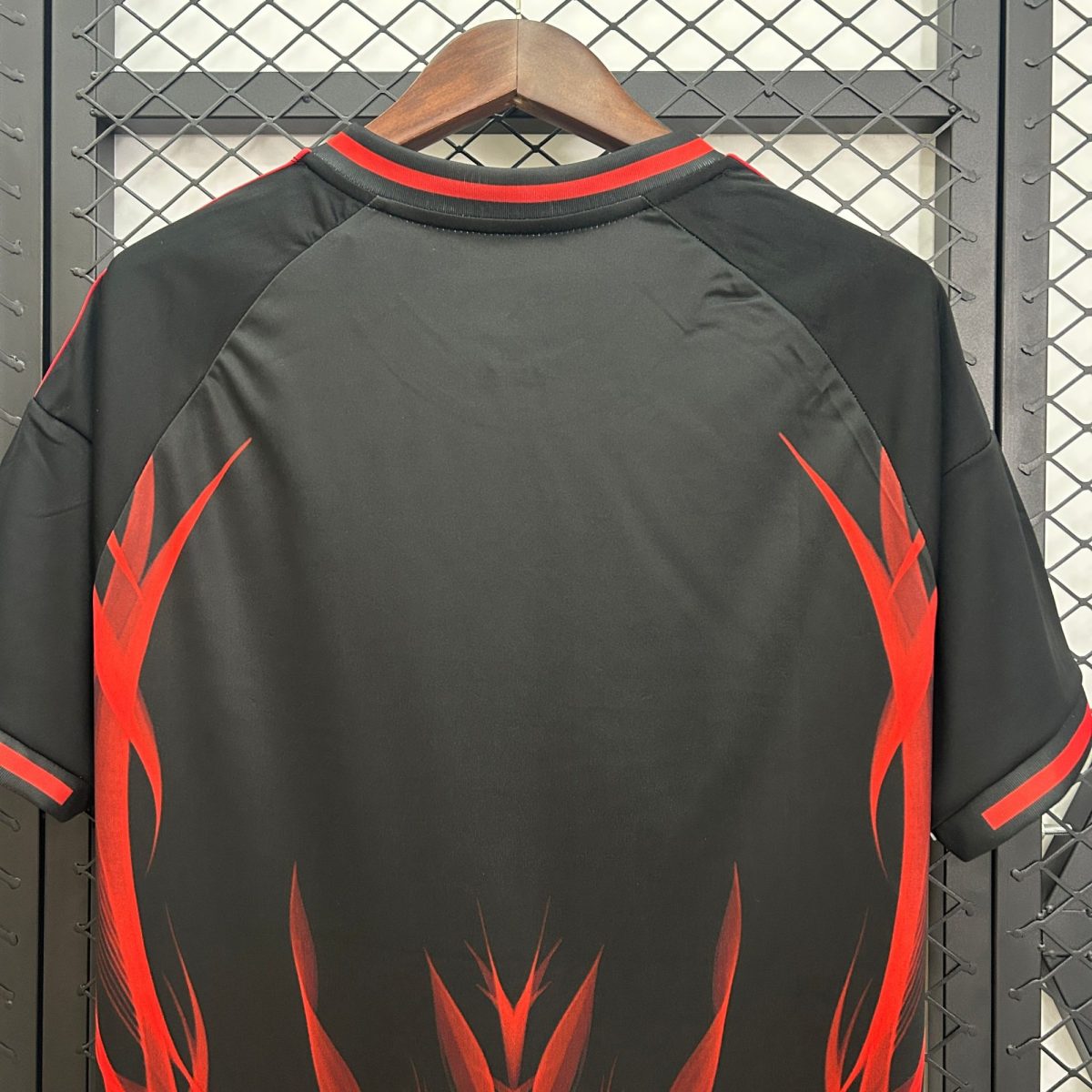 Black jacket with red flame graphics on a wooden hanger, hanging in front of a metal lattice background, seen from the back.