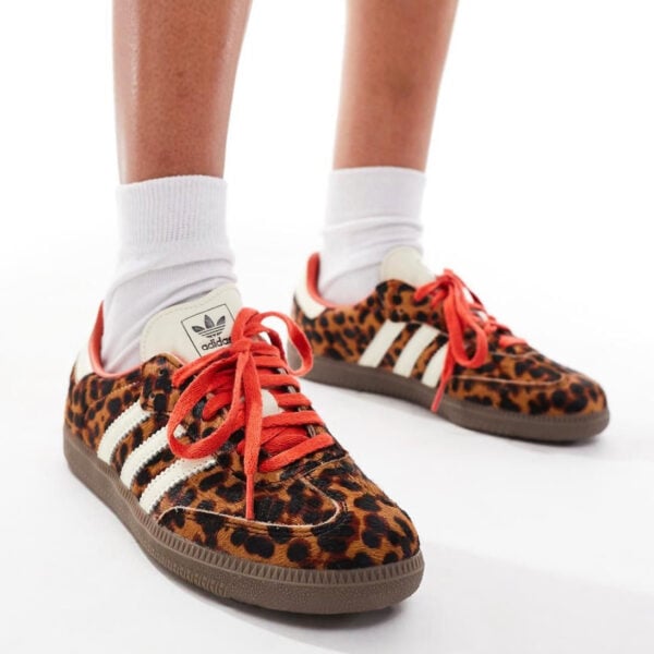 Feet wearing leopard-print Adidas sneakers with white stripes and red laces, paired with white socks.