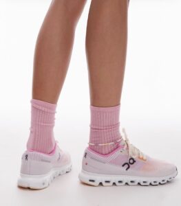 Pair of light pink athletic sneakers with white chunky sole, worn with pink ribbed socks on a model's legs.
