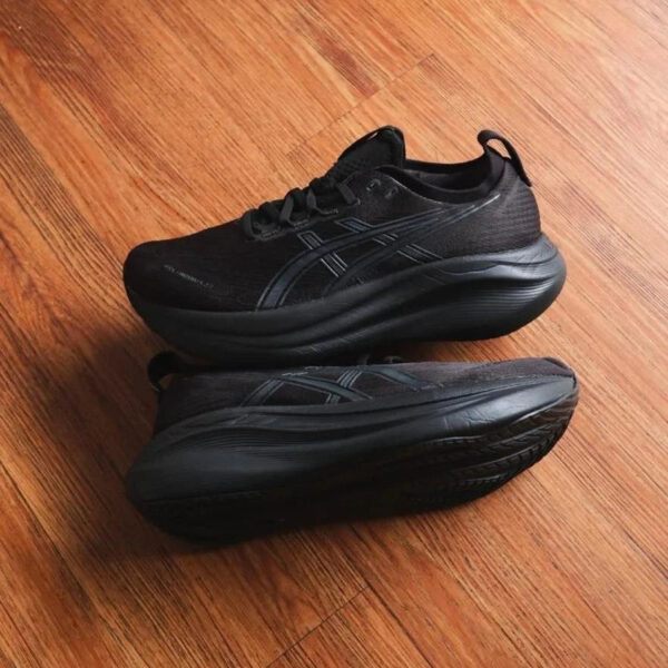 Two black running shoes stacked on a wooden floor, the top shoe resting on the bottom one with thick soles visible.