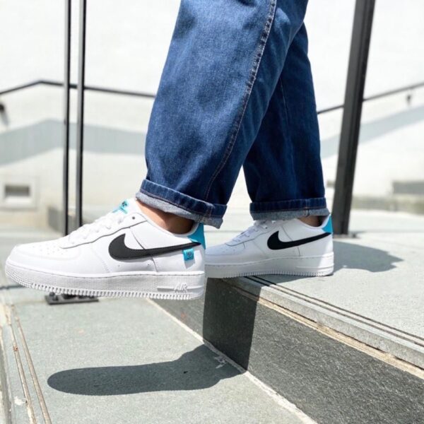 White Nike Air sneakers with a black swoosh, jeans cuffed, stepping on concrete steps outdoors.