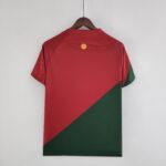 cdc063d5_9b5d5c2c-01ac-4f01-90b8-613ce590c041 | UAE SPORT STORE Back view of a red shirt on a wooden hanger, featuring a small yellow circular logo near the neckline.