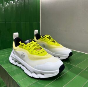 cdf0424b-82fa-4b7e-94bb-246559a69368 | UAE SPORT STORE Pair of bright yellow and white chunky sneakers with thick white sole on a green tiled display shelf, side logo visible.