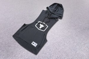 Dark gray sleeveless hoodie laid on a light carpet, with a drawstring hood and a white hex logo on the chest.