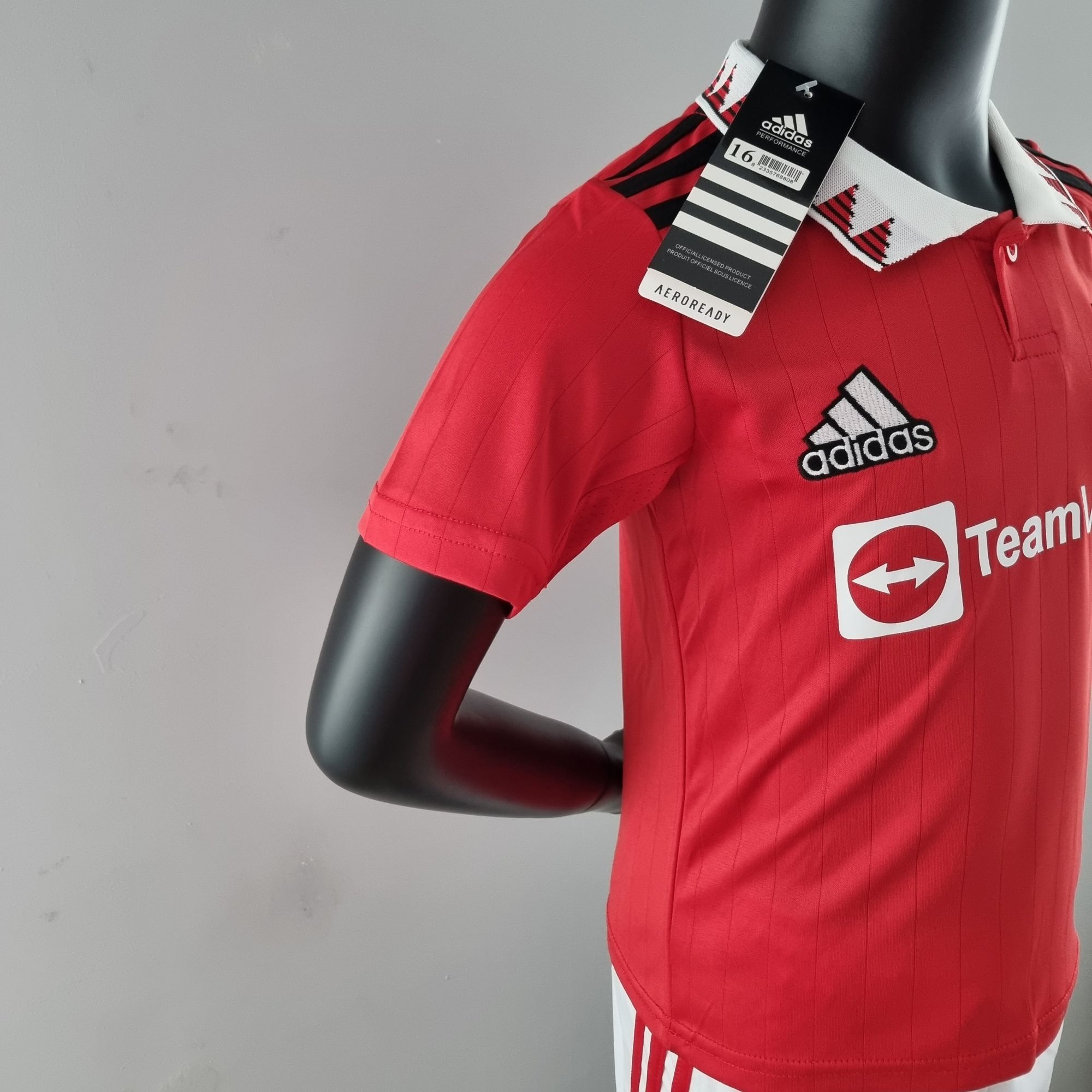 ce423c0f_4b8cbacd-90c7-4095-a1bb-ba19177c194e | UAE SPORT STORE Red Adidas sports jersey on a mannequin with a hanging product tag, showing the Adidas logo on the chest area and white collar detail.