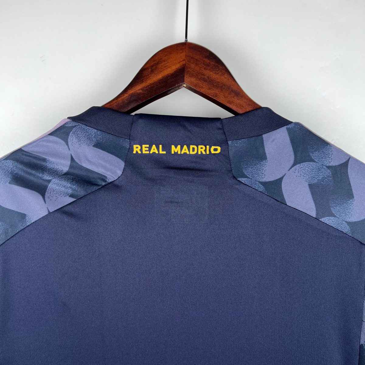 Wooden clothes hanger with a dark blue blazer hanging, Real Madrid letters visible on the back.