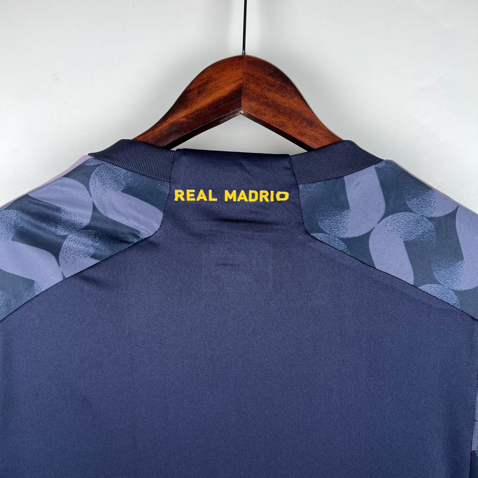 ce93df8c | UAE SPORT STORE Wooden clothes hanger with a dark blue blazer hanging, Real Madrid letters visible on the back.