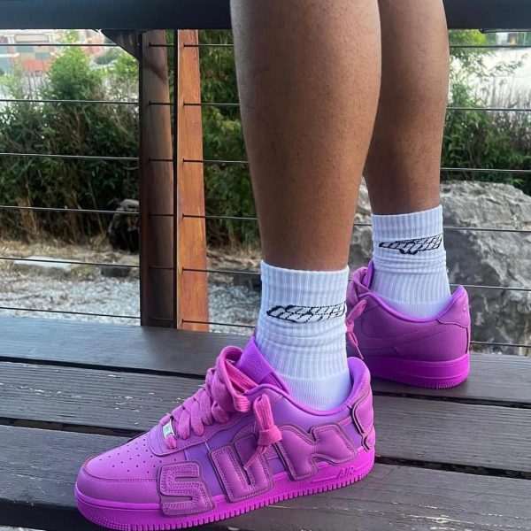 Person standing on a wooden deck wearing white socks and bright pink sneakers, outdoors with greenery in the background.