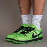 Bright neon green Nike sneakers with a black swoosh and white socks, standing on a gray background.