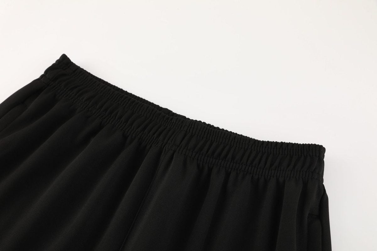 Close-up of black elastic waistband on smooth black fabric, showing shirred stitching and gathers.