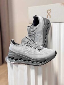 cef2c425-6f2e-4e74-80a0-ddcd43598fbb | UAE SPORT STORE Pair of gray running shoes with knit upper and sculpted midsole on a white display pedestal in a store, showing the ON logo on the side.