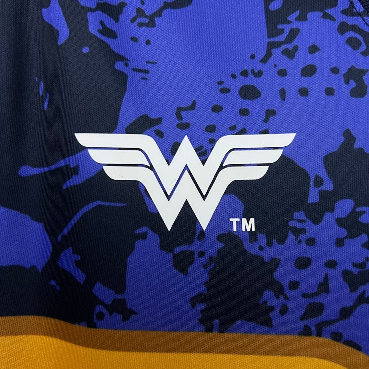 Close-up of blue fabric with a white winged 'W' logo and a yellow border along the bottom.