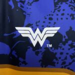 Close-up of blue fabric with a white winged 'W' logo and a yellow border along the bottom.