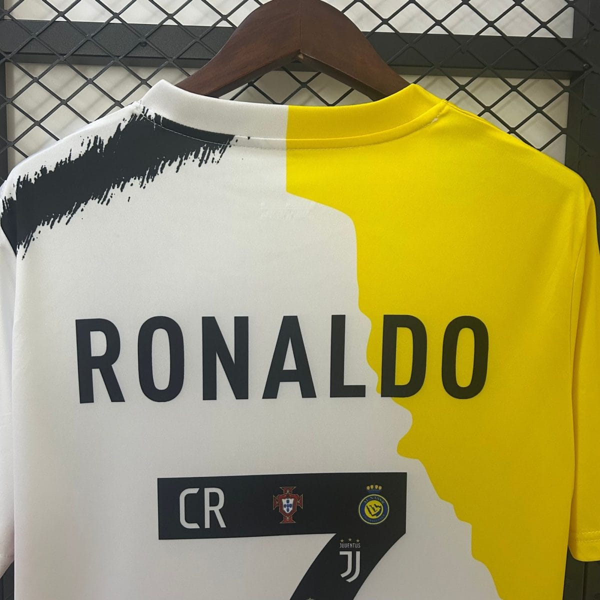 White and yellow Ronaldo jersey on a hanger, displaying the name 'RONALDO' and club logos on the chest area.