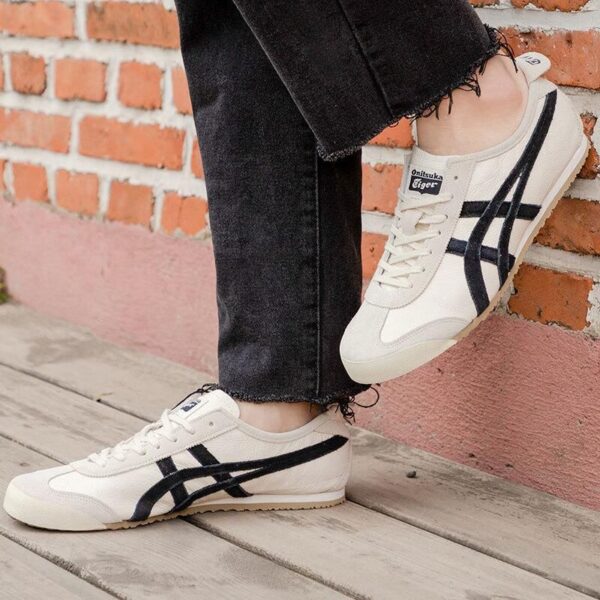 White sneakers with black side stripes worn with black jeans, photographed against a brick wall.