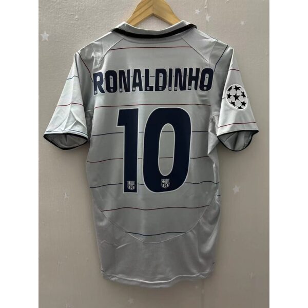 Gray soccer jersey with 'RONALDINHO' and the number 10 on the back hanging on a wooden hanger, showing a UEFA badge on the sleeve patch.