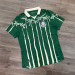 Green Palmeiras football jersey with white palm-tree stripes and white collar, laid flat on a wooden floor