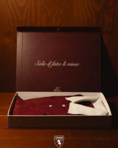 Open maroon gift box revealing a maroon shirt with a white tie on a wooden table; Torino FC badge visible at the bottom of the image.