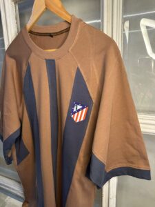 Brown long-sleeve shirt with dark blue vertical panels and a small Atlético Madrid crest patch on the chest