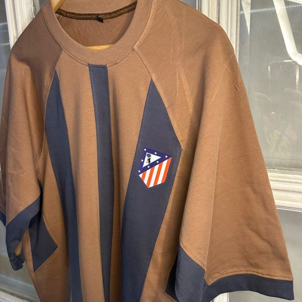 Brown long-sleeve shirt with dark blue vertical panels and a small Atlético Madrid crest patch on the chest