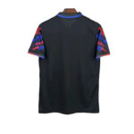 Back view of a black sports jersey with short sleeves featuring red and blue tie-dye patterns and blue trim at the collar.
