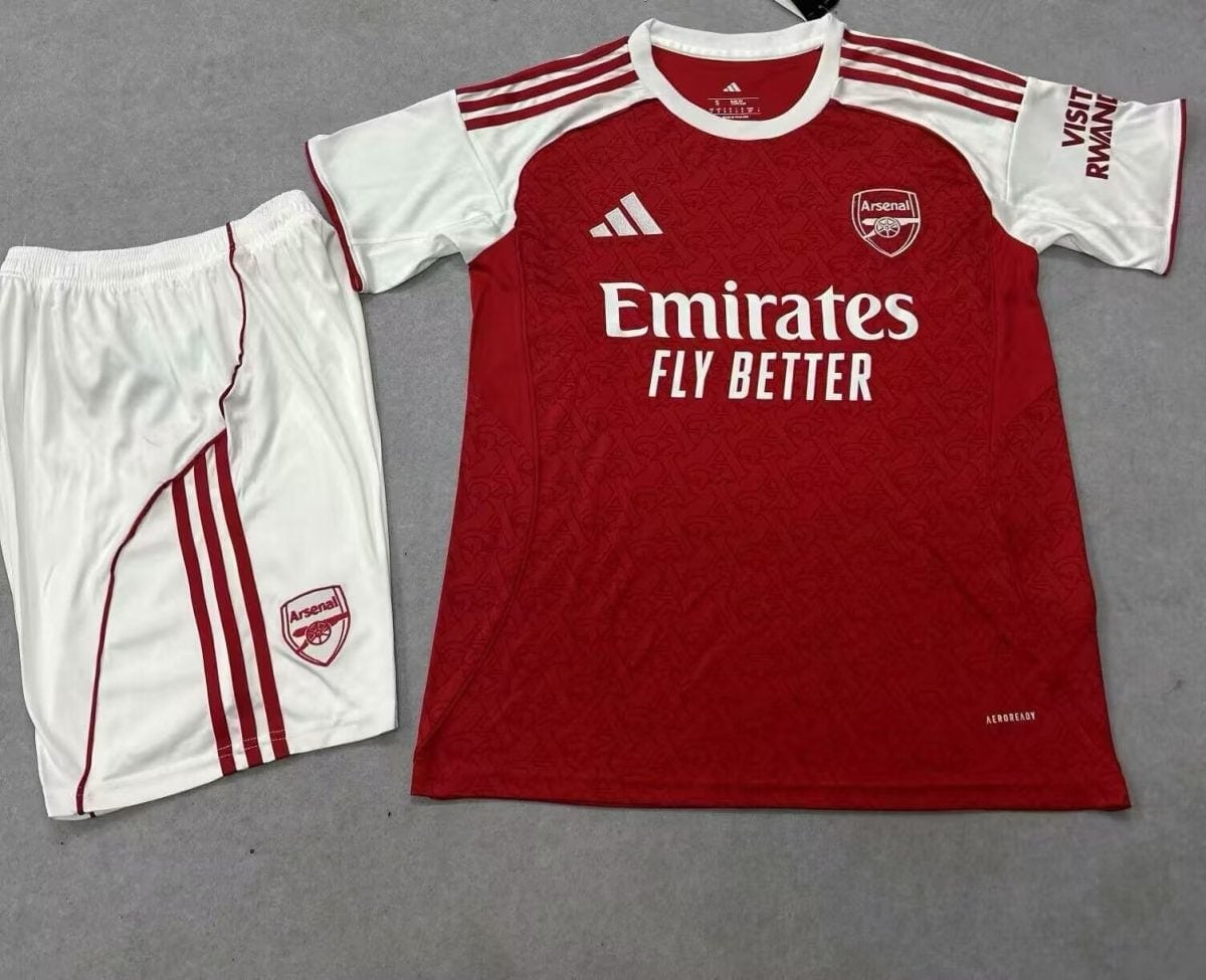 Arsenal home football kit laid flat: red shirt with white sleeves, crest, Adidas logo and Emirates Fly Better sponsor text, shorts beside with team crest.